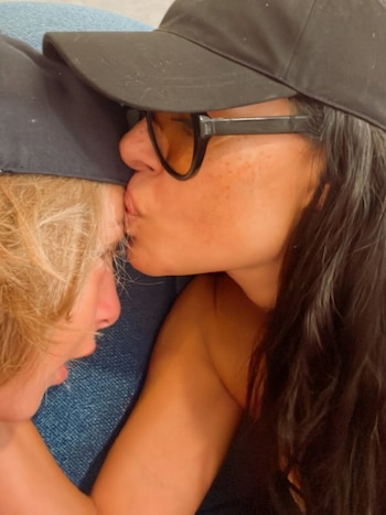 Primer plano de Galilea Montijo, con gorra negra y gafas de sol, besando la cabeza de su hijo rubio, que también lleva gorra, mostrando un momento de afecto