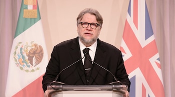 El director Guillermo del Toro, con barba y gafas, habla en un podio. Detrás de él se ven la bandera de México y la del Reino Unido.