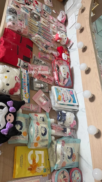 Mesa de madera con una variedad de productos Sanrio: peluches de Hello Kitty y Kuromi, maquillaje, relojes y artículos de papelería, al lado de un espejo con focos