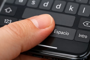 Primer plano de un dedo presionando el botón de la barra espaciadora que dice 'Espacio' en un teclado virtual negro en la pantalla de un smartphone.