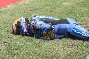 Un piloto de MotoGP, Alex Márquez, yace boca abajo en el césped vistiendo un mono de carreras azul y un casco multicolor tras una caída