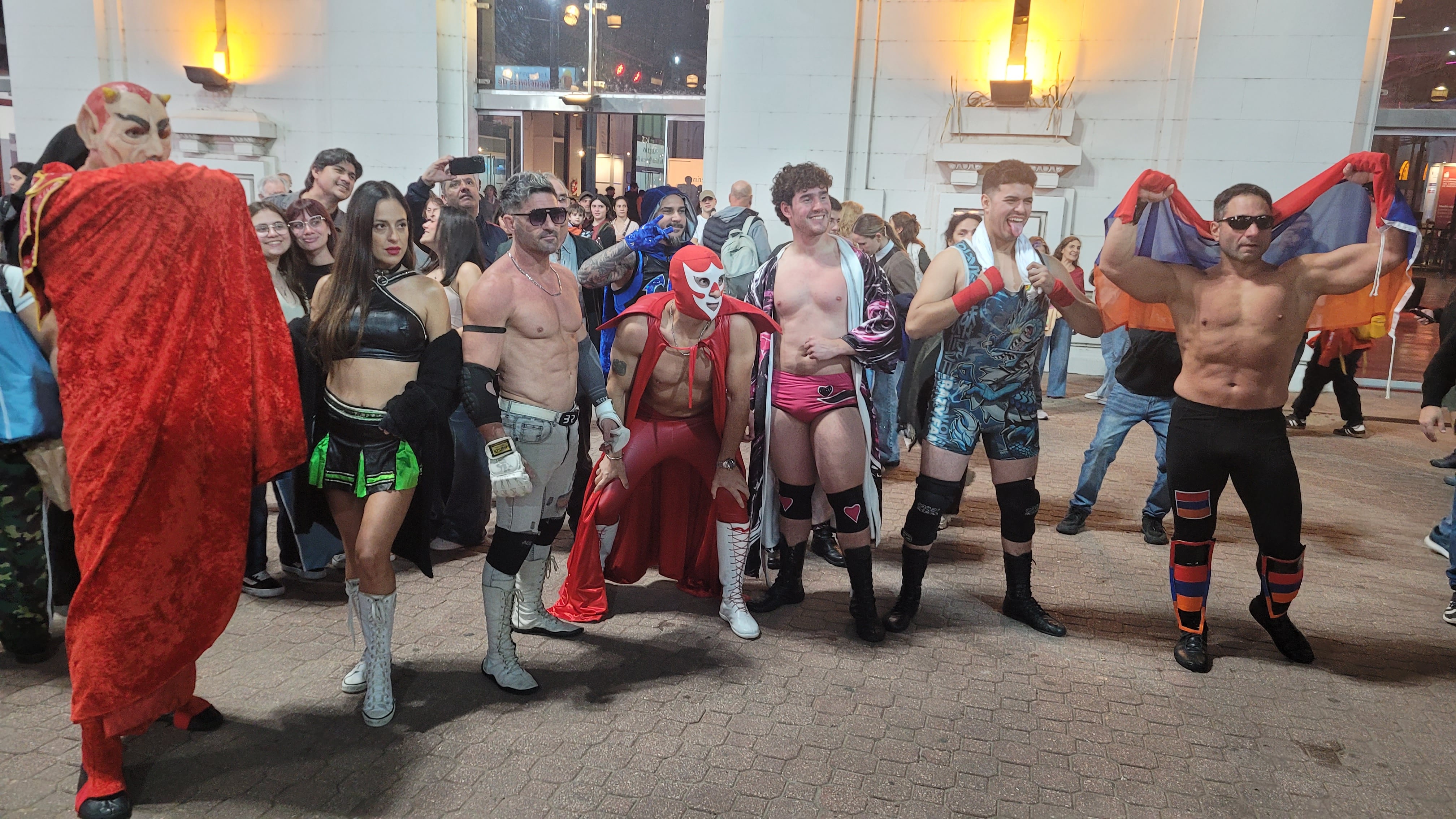 Un grupo de luchadores y personajes de Titanes en el Ring, incluyendo un diablo rojo y varios atletas en atuendos de lucha libre, posan durante su aparición en La Feria del Libro.