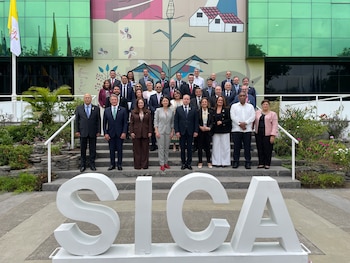 Catorce personas, hombres y mujeres, posan frente a un cartel de "25 Aniversario" en un vestíbulo moderno. El logo de SICA es visible en el balcón superior