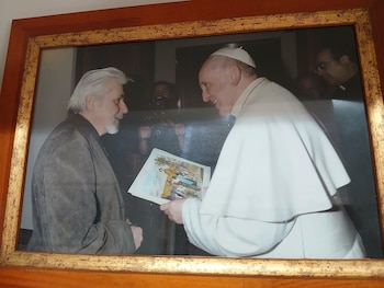 Fotografía enmarcada de Enrique Breccia y el Papa Francisco. El Papa, vestido de blanco, sostiene una pila de ilustraciones, mientras Breccia lo observa