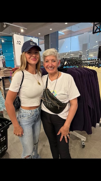 Eugenia Suárez, con gorra azul y camiseta blanca, posa junto a una mujer de cabello corto canoso en una tienda de ropa