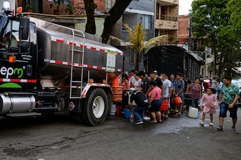 Un camión cisterna con el logotipo de epm aparcado en una calle mientras varias personas hacen fila con baldes y recipientes para recibir agua.