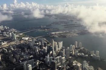 Vista aérea de Miami: rascacielos, puentes y una vasta bahía. El cielo azul con nubes blancas dispersas cubre la ciudad y el agua