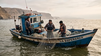 Tres hombres con chalecos salvavidas recogen una red con pocos peces a bordo de un bote de madera llamado La Esperanza frente a acantilados