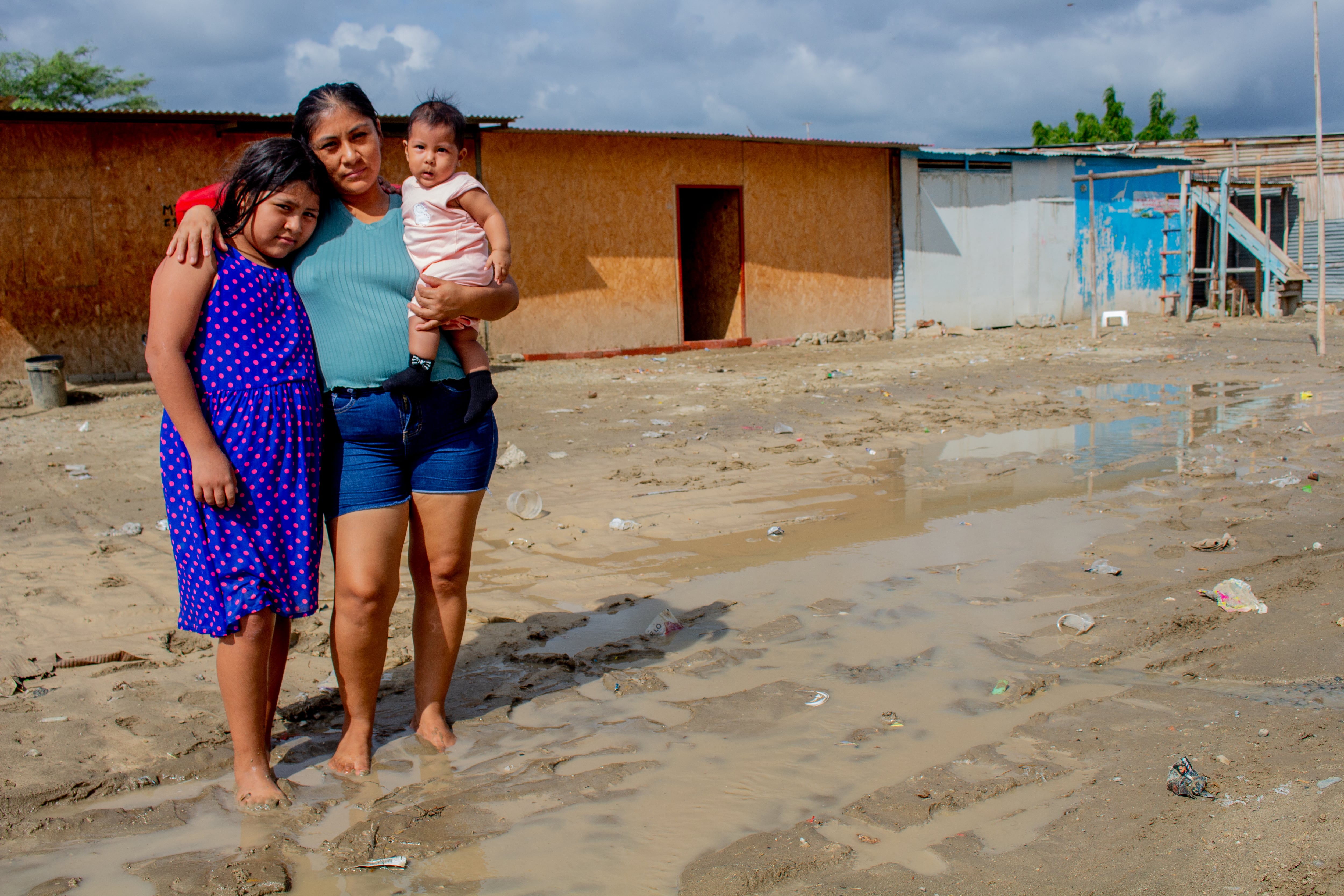 Una madre y sus dos hijos permanecen sobre una calle anegada en Piura, donde miles de niñas y niños viven en zonas de riesgo alto ante las lluvias vinculadas al fenómeno El Niño. (UNICEF)