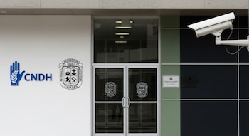 Entrada de edificio gubernamental con puertas de vidrio y placas institucionales. Logos de CNDH y Fiscalía de Chiapas visibles. Cámara de vigilancia en la parte superior derecha.