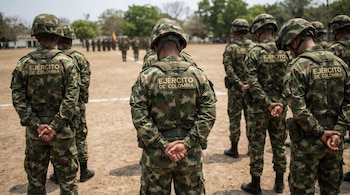Varios militares del Ejército de Colombia, de espaldas, con uniformes de camuflaje, de pie en una formación en un campo abierto. No se ven sus caras.