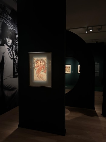 Un cuadro ilustrado colgado en una pared negra junto a una fotografía en blanco y negro y un panel con apertura circular