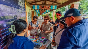 Personas reunidas alrededor de una mesa con mapas y folletos turísticos en un pasillo techado con banderas de Guatemala colgadas
