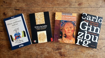 Vista aérea de cuatro libros con portadas variadas, de color oscuro, azul y naranja, colocados sobre una mesa de madera rústica.