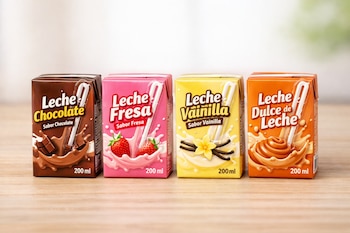 Cuatro envases pequeños de leche con popotes en fila sobre una mesa de madera. Los sabores son chocolate, fresa, vainilla y dulce de leche, cada uno de 200 ml.