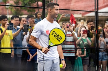 Cristiano Ronaldo en una cancha de pádel con una pala amarilla y una pelota, rodeado de público que sostiene teléfonos móviles