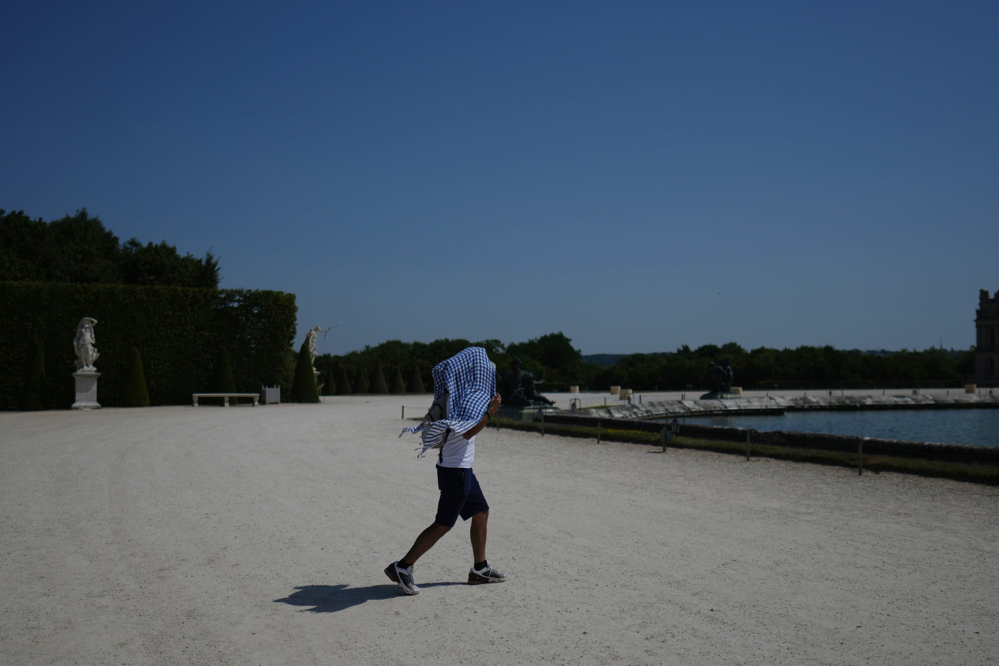 Un hombre se cubre del sol con un pañuelo en los jardines de Versalles, cerca de París, el 22 de junio de 2026, en medio de la ola de calor que afecta a Francia. (Foto AP/Thibault Camus)