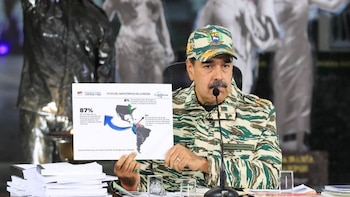 Nicolás Maduro, vestido con uniforme militar y gorra, sentado en un podio con un micrófono, sosteniendo un gráfico con un mapa de rutas del narcotráfico