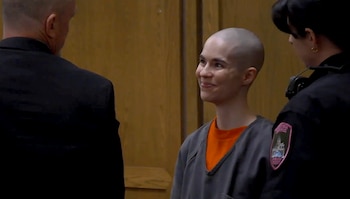 Alyssa Bradburn, con la cabeza rapada y vestida con uniforme de prisión, sonríe entre un abogado y una oficial de policía en un juzgado