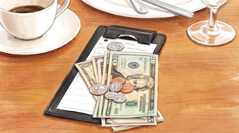 Billetes de dólares y monedas sobre un portacuentas negro junto a una taza de café, un plato y una copa en una mesa de madera.