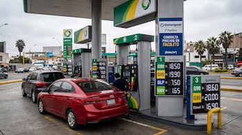 Un automóvil rojo junto a surtidores de combustible con carteles digitales de precios y un cartel con el logotipo de Osinergmin.