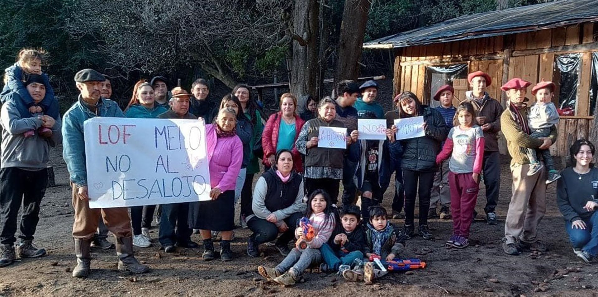 Miembros de la comunidad Mapuche Lof Melo, incluyendo hombres, mujeres y niños, se manifiestan en Neuquén con pancartas para expresar su rechazo al desalojo de sus tierras ancestrales.