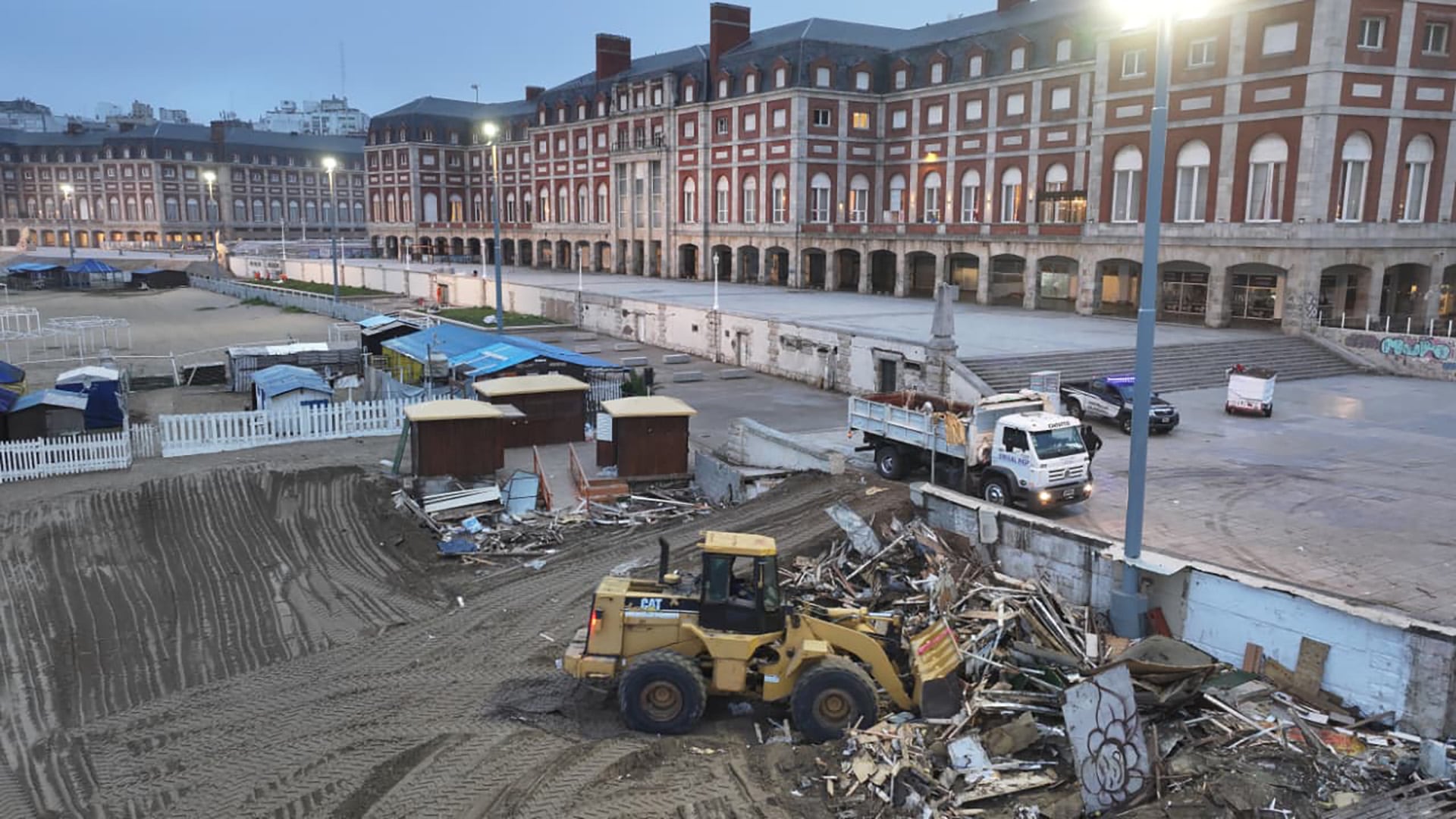 Una pala cargadora amarilla trabaja en la remoción de escombros en el predio ferial La Bristol de Mar del Plata, con el icónico edificio en el fondo.