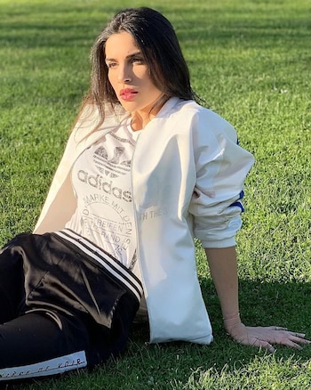 Suhaila Jad sentada sobre el césped verde, con una camiseta blanca, chaqueta blanca y pantalón negro, con el sol iluminando su rostro