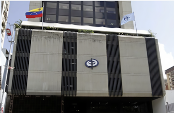 Fachada de un edificio de concreto gris con paneles verticales oscuros, un logo azul y blanco de "MP", y las banderas de Venezuela y del Ministerio Público