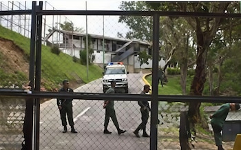 Militares uniformados en un camino junto a una patrulla blanca, observados a través de una cerca metálica frente a un edificio