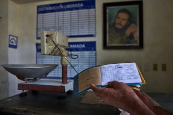 Un hombre muestra su cartilla de racionamiento, conocida como "libreta", mientras al fondo se ve una imagen enmarcada de Fidel Castro, en una bodega estatal en La Habana, Cuba, el sábado 2 de mayo de 2026. (AP Foto/Ramón Espinosa)