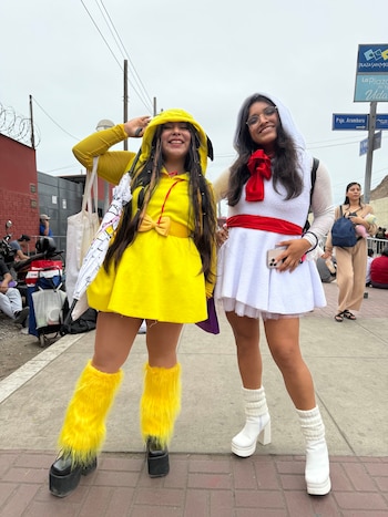 Dos jóvenes vestidas con trajes amarillos y blancos posan sonrientes en una acera junto a carteles de señalización vial