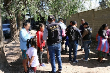 Agentes con chalecos del Sistema Penitenciario conversan con personas y niños junto a unos árboles y una pared de bloques