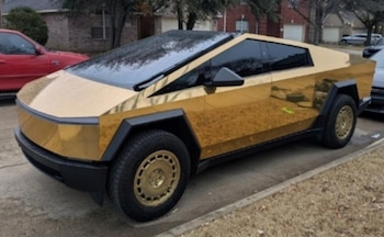 Un vehículo Tesla Cybertruck con acabado dorado brillante y rines dorados está estacionado en una calle residencial
