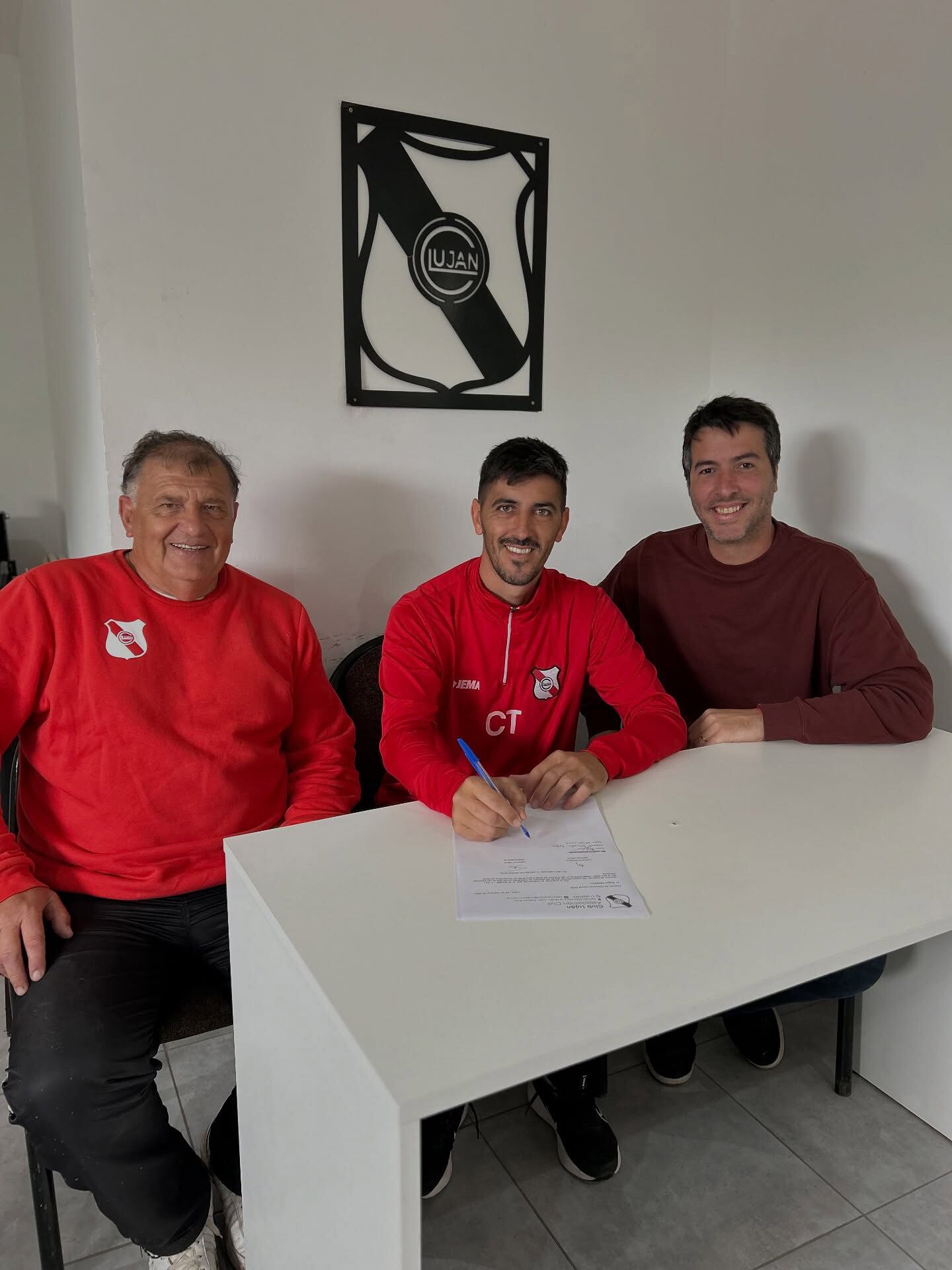 Santiago Fredes (en el medio) firma su contrato como técnico de Luján. A su izquierda, el presidente Federico Vanin (Instagram @clublujan.oficial)