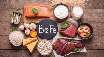 Salmón, sardinas, camarones, carne, hígado, arroz, leche, yogur, queso, champiñones, yemas de huevo y cápsulas. Pizarra con B12 Fe sobre mesa de madera.