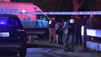 Oficiales de policía y vehículos de emergencia permanecen detrás de una cinta de seguridad en una calle nocturna