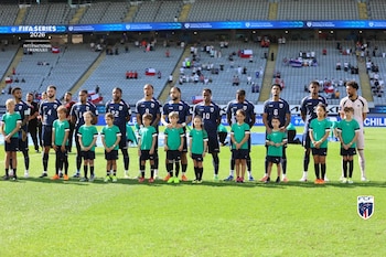 Jugadores de Cabo Verde y niños con uniformes verdes posan en el campo. Gradas del estadio con banderas chilenas visibles al fondo