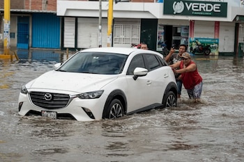 Tres hombres empujan un automóvil blanco detenido en una calle anegada frente a varios edificios comerciales