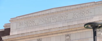 Parte superior de la fachada de piedra de un edificio con el grabado Benson Polytechnic School bajo un cielo despejado