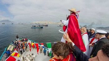 Vista aérea de una estatua de San Pedrito con capa roja en un barco decorado, rodeado de numerosas embarcaciones pesqueras y personas en el mar de Chimbote, Perú