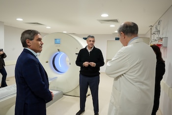 Tres personas dialogan en una sala médica frente a un tomógrafo grande de color blanco con luz azul en su interior