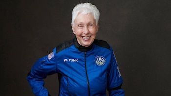 Retrato de mulher de cabelos brancos e sorriso largo, usando vestido azul claro mostrando um patch com a bandeira americana e o nome W. FUNK