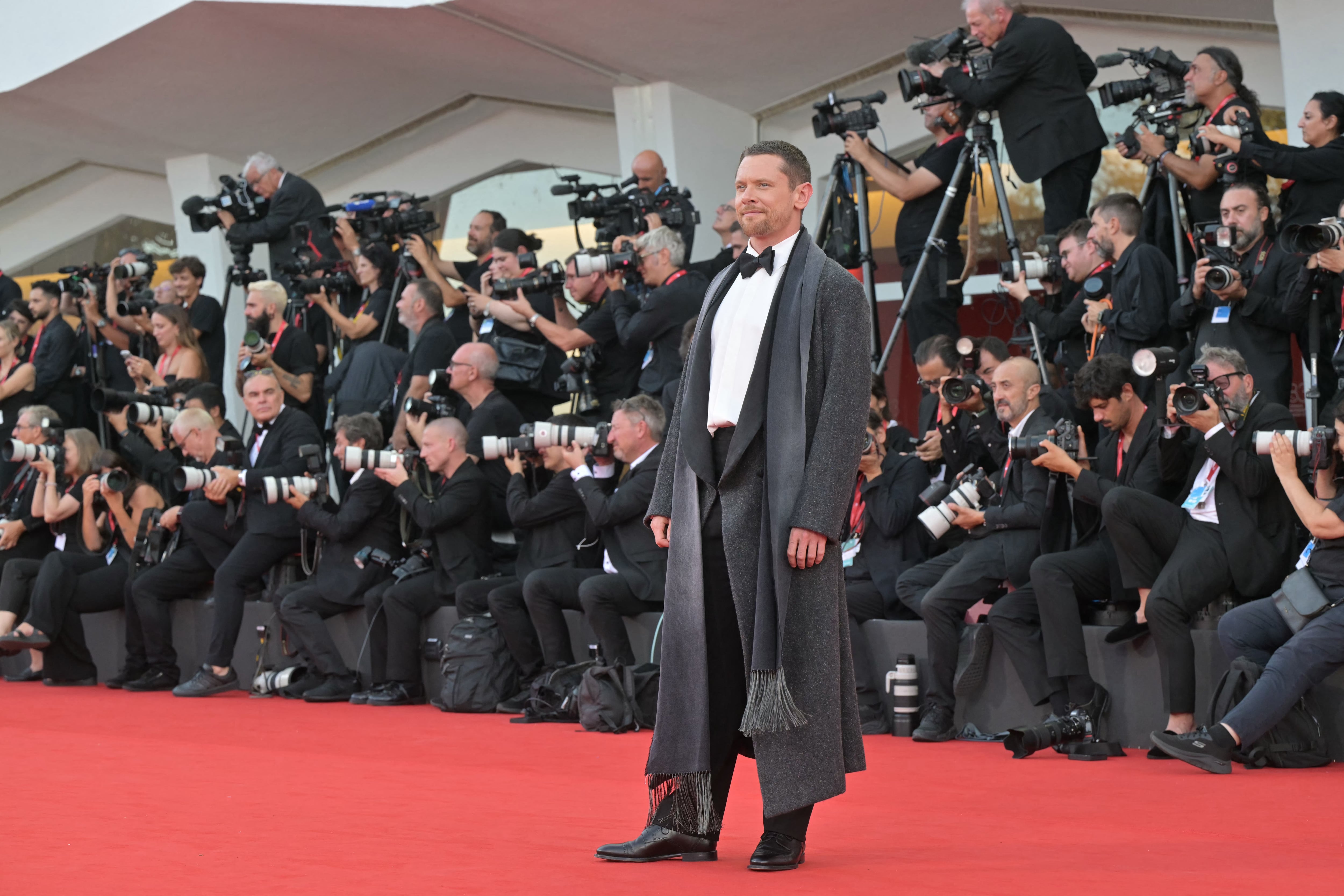 Jack O’Connell con esmoquin negro y abrigo gris oscuro con flecos (Photo by Stefano RELLANDINI / AFP)