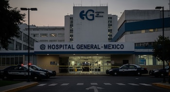 Edificio con letrero "Hospital General - Mexico" y logo "EG", entrada principal con cinta amarilla de seguridad, dos patrullas de policía estacionadas.