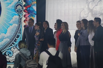 Un grupo de hombres y mujeres elegantes posa en fila en un escenario frente a una pantalla de fondo ilustrada