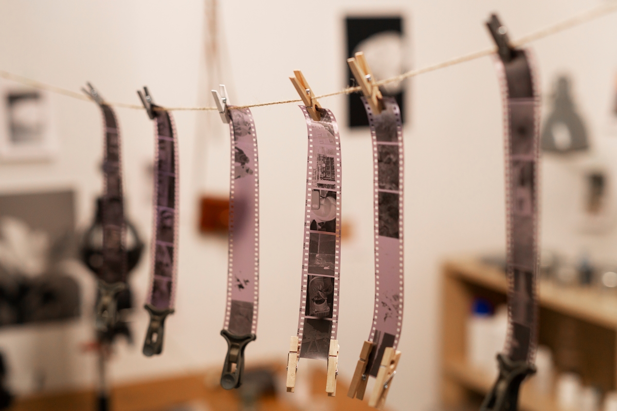 Primer plano de varias tiras de película fotográfica, colgadas de una cuerda con pinzas de madera y de plástico negro