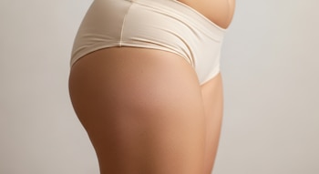 Muslo, cadera y abdomen parcial de una mujer con ropa interior beige, piel de tono medio y textura visible.