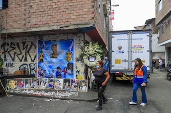 Un memorial callejero con fotografías de diez personas, una pancarta azul, velas, una corona floral y un camión de ayuda humanitaria