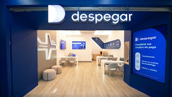 Interior de una tienda Despegar con paredes azules y blancas, el logotipo iluminado, múltiples pantallas y escritorios con laptops para atención al cliente
